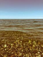 bellissimo multicolore il giro pietre su il mare, fiumi, laghi, stagno, oceano e bollente acqua con onde su il roccioso spiaggia di un' tropicale caldo ricorrere su il orizzonte e cielo. verticale Visualizza foto