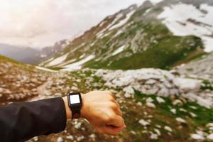 mano viaggiatore indossare e guardare a il inteligente orologio alto nel il montagne. moderno tecnologie foto