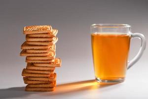 un' pila di d'oro Grano biscotti e un' boccale di fragrante verde tè nel su un' grigio sfondo. biscotti di cui su nel un' prima colazione colonna e un' d'oro evidenziare con tè tazze foto