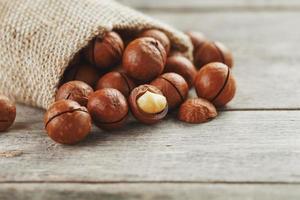 macadamia noccioline rovesciato su di il Borsa su un' di legno sfondo avvicinamento con uno pelato Noce foto