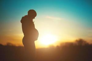 silhouette di un' futuro mamma, incinta donna rilassare nel il parco su un' tramonto sfondo foto