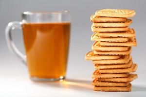 un' pila di d'oro Grano biscotti e un' boccale di fragrante verde tè nel su un' grigio sfondo. biscotti di cui su nel un' prima colazione colonna e un' d'oro evidenziare con tè tazze foto