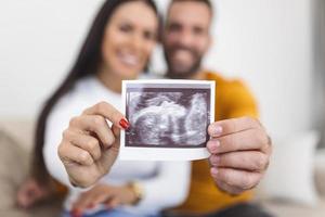 donna e sua fidanzato Tenere su un Immagine di sua ecografia di il bambino. giovane contento coppia con bambino ultrasuono foto