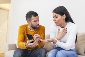 arrabbiato coppia o matrimonio combattente per un' mobile Telefono a casa. geloso caucasico uomo Tenere inteligente Telefono e mostrando Messaggio per il suo moglie