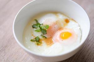 uovo prima colazione , bollito uova su bianca ciotola con Pepe, coriandolo su di legno tavolo, onsen tamago uovo - uovo microonde foto