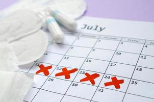 mestruale pastiglie e tamponi su mestruazione periodo calendario con rosso attraversare votazione bugie su lilla sfondo foto