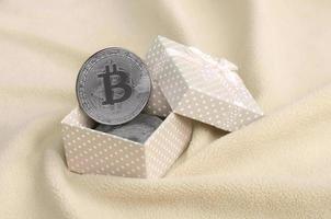 il argento bitcoin bugie nel un' piccolo arancia regalo scatola con un' piccolo arco su un' coperta fatto di morbido e soffice leggero arancia vello tessuto con un' grande numero di sollievo pieghe foto