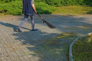 un' donna spazza caduto le foglie con un' scopa su il strada. il comunale servizio monitor il pulizia nel il città. foto