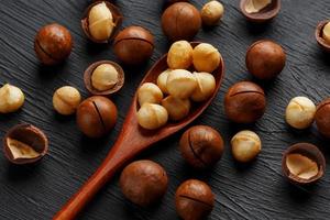 sgusciate macadamia Noce e pelato macadamia Noce su un' nero strutturale sfondo nel un' di legno cucchiaio foto