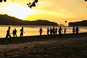 silhouette gruppo di persone giocando il calcio su il spiaggia nel il tramonto con paesaggio marino e montagna nel sfondo foto