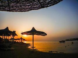 sorprendente tramonto su il spiaggia con sole ombrelli foto