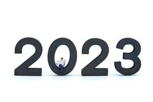2023 attività commerciale nuovo anno concetto. avvicinamento di uomo d'affari miniatura figure seduta e lettura un' giornale su di legno numero su bianca sfondo. foto