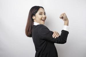 eccitato asiatico attività commerciale donna indossare un' nero completo da uomo mostrando forte gesto di sollevamento sua braccia e muscoli sorridente con orgoglio foto