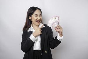 un' contento giovane donna d'affari è indossare nero completo da uomo e Tenere denaro contante i soldi nel indonesiano rupia isolato di bianca sfondo foto