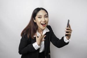 sorpreso asiatico donna d'affari indossare nero completo da uomo Tenere sua smartphone, isolato di bianca sfondo foto