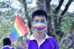 ritratto asiatico giovane ragazzo detiene arcobaleno bandiera, lgbt simbolo, nel mani mentre unendo il suo lgbt attività a scuola, concetto per lgbt Comunità celebrazione nel orgoglio mese, giugno, 2023, in giro il mondo. foto