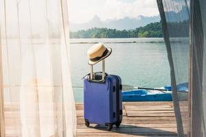 tempo per viaggio e relax, viaggio valigia con cappello in piedi su il pavimento su il Camera da letto a il lago e spiaggia. foto