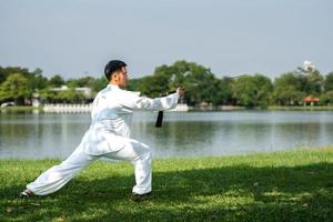 giovane uomo praticante tradizionale tai chi spada, tai ji nel il parco per sano, tradizionale Cinese marziale arti concetto su naturale sfondo . foto