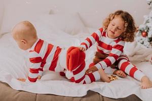 bambini nel rosso e bianca pigiama provare su divertente bicchieri con Santa Claus seduta nel letto. stile di vita. fratello e sorella festeggiare Natale. ragazzo e ragazza siamo giocando a casa. alto qualità foto