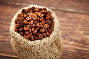 appena arrostito aromatico caffè nel un' tela ruvida Borsa su un' di legno sfondo. foto