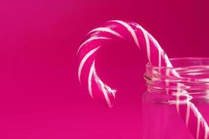 uno lecca-lecca caramella canna nel un' bicchiere vaso su un' rosa sfondo. foto