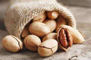 Noci Pecan versare su di un' Borsa su un' di legno tavolo, avvicinamento. pelato, nel un' guscio. foto