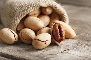 Noci Pecan versare su di un' Borsa su un' di legno tavolo, avvicinamento. pelato, nel un' guscio. foto