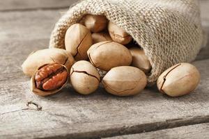 Noci Pecan versare su di un' Borsa su un' di legno tavolo, avvicinamento. pelato, nel un' guscio. foto