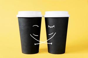 amorevole coppia di caffè tazze. abbracciare monouso caffè tazze su un' giallo sfondo. creativo concetto di romantico relazioni foto