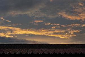 rosso tetto di un vecchio Casa sotto il cielo e arancia mattina nuvole. foto