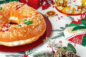 roscon de Reyes con crema e Natale ornamenti su un' rosso piatto. re giorno concetto spagnolo tre re torta.tipica spagnolo dolce per Natale foto