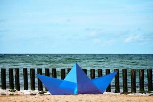 origami blu carta barca su sabbioso spiaggia per disegno, blu carta nave su mare costa. bellissimo orizzonte foto