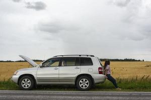 un' rotto macchina. un' giovane donna sta su il strada di un' rotto auto contro il sfondo di un' giallo campo. foto