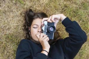 carino adolescente ragazza con un' telecamera, un' ragazza assunzione immagini su un' retrò Vintage ▾ telecamera su il erba nel il parco, un' passatempo concetto foto