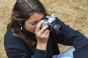 carino adolescente ragazza con un' telecamera, un' ragazza assunzione immagini su un' retrò Vintage ▾ telecamera su il erba nel il parco, un' passatempo concetto foto