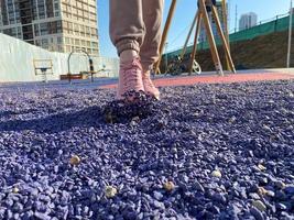 un' giovane bellissimo snello donna nel un' rosa tuta da ginnastica e scarpe da ginnastica passeggiate su viola pietre e ghiaia nel il gli sport campo nel il cortile di il Casa foto