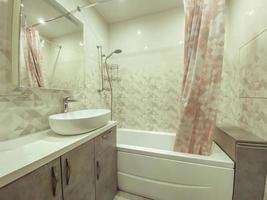 moderno, elegante bagno nel un' Residenziale appartamento. un' enorme Lavello fatto di bianca Materiale, un' pietra controsoffitto. specchio con scaffali doccia dietro a un' tenda foto