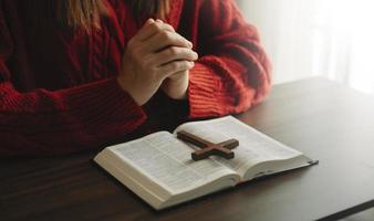 mani insieme in preghiera a Dio insieme alla Bibbia nel concetto cristiano e nella religione, la donna prega nella Bibbia sul tavolo di legno foto