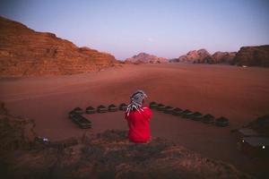 donna turista nel vestito sedersi su scogliera a punto di vista su tramonto nel wadi Rum deserto - valle wadi saabit. Giordania Esplorare concetto foto