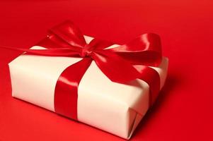 un' regalo scatola con grande rosso arco contro rosso sfondo. vacanze concetto foto