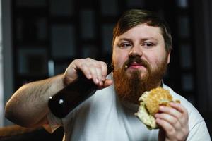 l'uomo grasso guarda la tv, mangia hamburger e beve birra foto