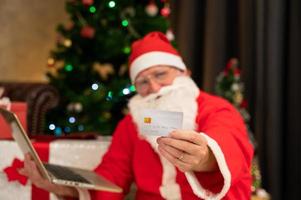 Santa Claus indossare rosso costume fare Natale in linea shopping con credito carta su il computer portatile a casa foto