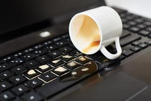 versare caffè a partire dal bianca tazza su il computer il computer portatile tastiera foto