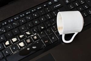 versare caffè a partire dal bianca tazza su il computer il computer portatile tastiera foto