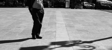 siciliano uomo nel un' piazza con il suo mani nel il suo tasche con allungata ombra nel nero e bianco nero e bianca. ombra e luce, uomo silhouette foto