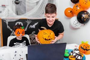 contento giovane ragazzi, fratelli parlando con nonni o amici attraverso video chiamata utilizzando il computer portatile su Halloween giorno , eccitato ragazzo mostrando il suo nuovo Jack o' lanterna Halloween zucca con lavorato Sorridi foto