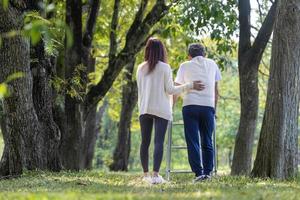 asiatico anziano padre con camminatore e figlia a piedi insieme nel il parco durante estate per leggero esercizio e fisico terapia uso foto