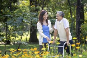 asiatico anziano padre con camminatore e figlia a piedi insieme nel il parco durante estate per leggero esercizio e fisico terapia uso foto
