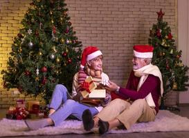 anziano caucasico coppia festeggiare Natale insieme nel felicità e eccitazione a casa con rosso Santa cappello e Natale albero foto