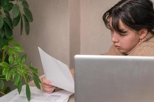 ragazza lavori con documenti seduta nel davanti di un' il computer portatile a sua scrivania foto